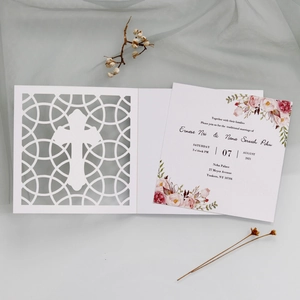 Detail of laser-cut white invitation card featuring a golden cross and floral inner page