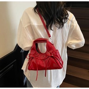 Sac à main en cuir verni rouge avec nœuds porté par un mannequin en intérieur