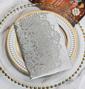 Detail of silver glitter laser cut wedding invitation with floral patterns on a plate