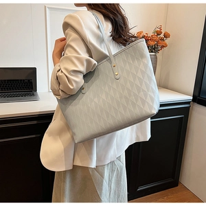 Detail of light blue quilted tote bag with gold rivets worn by a model in office setting