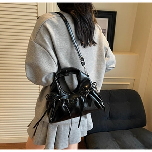 Détail d'un sac à main en cuir verni noir avec nœud décoratif et bandoulière amovible
