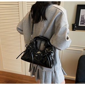 Détail d'un sac à main noir brillant avec poignée ronde et nœuds élégants sur les côtés