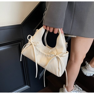 Détail d'un sac à main blanc cassé brillant avec nœuds et texture plissée latérale