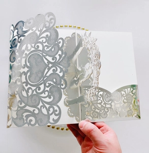 Detailed laser-cut silver wedding invitation with intricate floral heart patterns