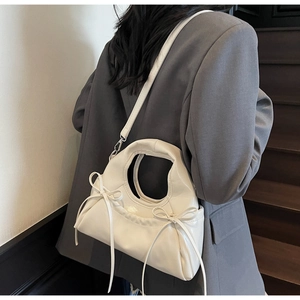 Détail d'un sac bandoulière crème avec nœuds délicats et plis souples en cuir souple