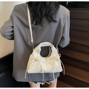 Détail d'un sac à bandoulière blanc brillant avec nœuds porté par un mannequin