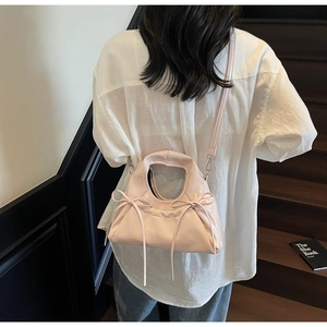 Détail du sac à main rose plissé avec grands nœuds sur une tenue chemise blanche