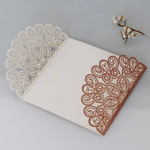Macro detail of laser-cut lace floral pattern with rose gold glitter on wedding invitation
