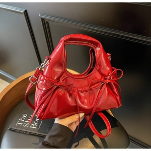 Détail du sac à main en cuir verni rouge avec nœuds décoratifs et bandoulière réglable