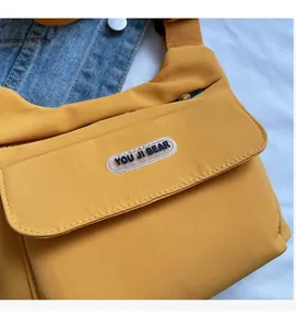 Dettaglio della borsa a tracolla in nylon giallo con logo YOU JI BEAR su denim