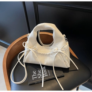 Détail du sac à main blanc crème avec nœud décoratif sur un fond noir élégant