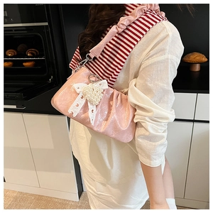 Detail of pink pleated crossbody bag with lace bow and pearl heart charm on a woman