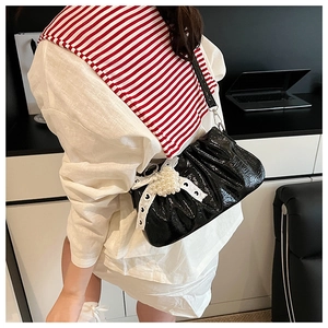 Detail of black patent leather crossbody bag with white lace and pearl bow decoration