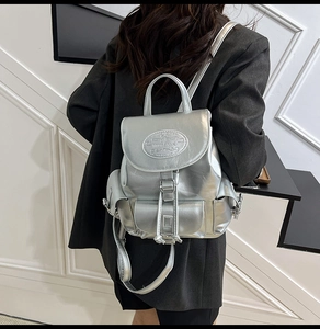 Sac à dos argenté métallisé avec rabat à cordon, porté par un mannequin en blazer sombre
