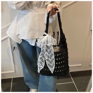 Detail of hand-woven black crochet bag featuring a large white lace bow and drawstring liner