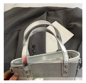 Detailansicht der silbernen Beuteltasche mit Metallgriffen und Nieten auf grauem Anzug
