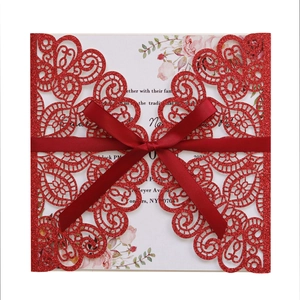 Detail of red glitter laser-cut wedding invitation with satin bow and floral inner card