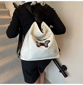 Detail of a creamy white nylon backpack with a striped dachshund embroidery and black straps