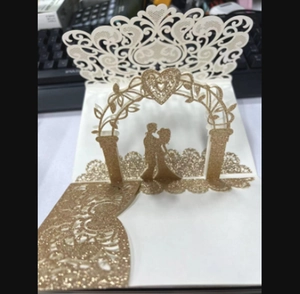 Intricate laser-cut wedding invitation with gold glitter arch and couple silhouette