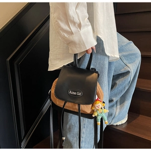Detail eines Mini-Strohrucksacks mit schwarzer Lederklappe und Comic-Puppenanhänger