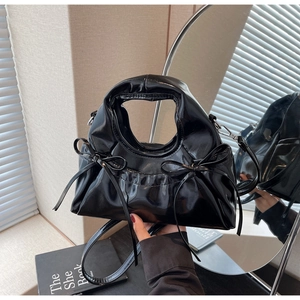 Détail d'un sac à main noir brillant en cuir verni avec nœuds latéraux et poignée