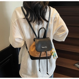 Detail eines Mini-Strohrucksacks mit Lederklappe und Acme-Girl-Logo auf Holztreppen