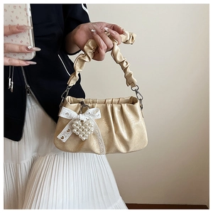Detail of beige pleated cloud bag with pearl heart pendant and lace bow accessory