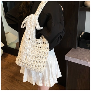 Detail view of woven shoulder bag featuring a large lace bow and hollow mesh texture