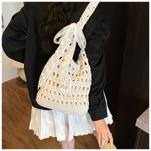 Close-up of woven shoulder bag featuring delicate white lace bow ribbon and embroidery