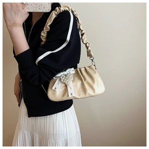 Detail of a creamy pleated shoulder bag featuring a pearl pendant and a silk bow