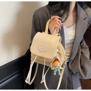 Detail eines Mini-Stroh-Rucksacks mit Acme Girl Prägung und süßem Puppenanhänger