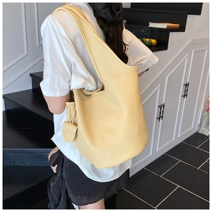 Chic cream yellow pebbled leather bucket bag with signature pendant worn on shoulder