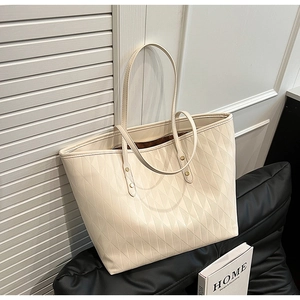 Detail of quilted creamy white tote bag showing embossed pattern and golden metal rivets