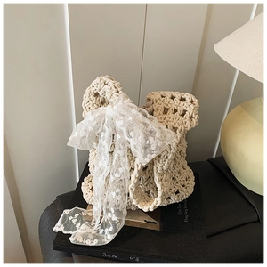 Detailed close-up of ivory woven bucket bag featuring large white lace bow and knit texture