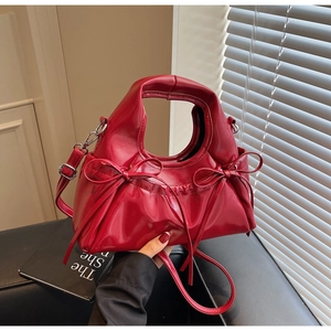 Détail d'un sac à main rouge brillant avec nœud décoratif et bandoulière réglable