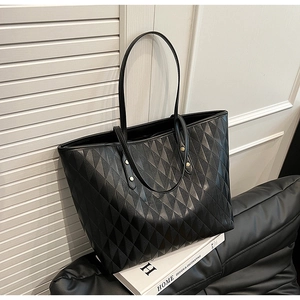 Detail of black quilted tote bag with gold metal studs and slim leather shoulder straps