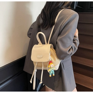 Detail eines Stroh- und Lederrucksacks mit Acme Girl Metallemblem auf der cremefarbenen Klappe
