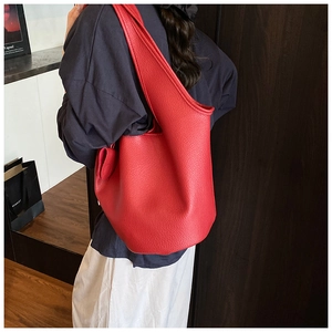 Detail of red pebbled leather bucket bag featuring wide shoulder strap and soft texture