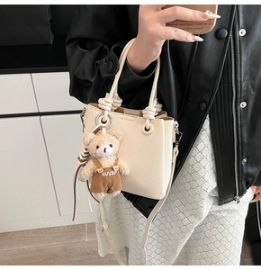 Detail of off-white lychee grain leather mini bucket bag with a plush bear charm accessory