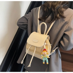 Detail eines Stroh-Rucksacks mit weißer Lederklappe und süßem Mädchenpuppen-Anhänger