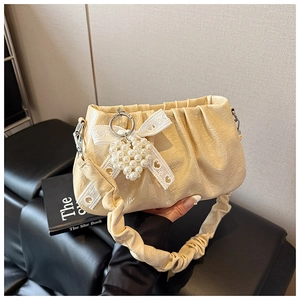 Détail du sac beige plissé avec breloque cœur perlé et nœud en dentelle sur sofa en cuir