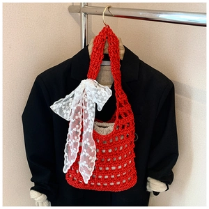 Detail of red woven bucket bag featuring a large white lace bow and hollow mesh texture
