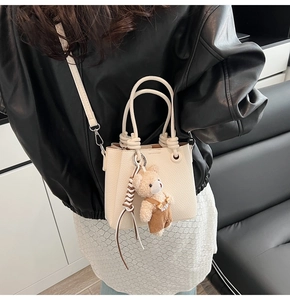 Detail of cream pebbled leather bucket bag with teddy bear charm and braided drawstring
