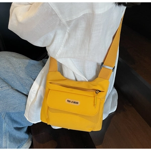 Dettaglio della borsa a tracolla in tela giallo brillante indossata su camicia bianca