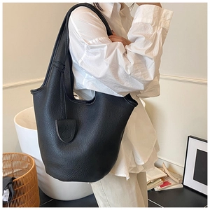 Close-up of a large black textured leather bucket bag carried on the shoulder by a model