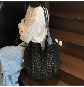 Détail d'un sac cabas en maille noire avec bandoulière en cuir porté par un mannequin