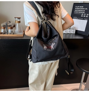Detail of black nylon backpack featuring a sequin dog patch and gold hardware on model