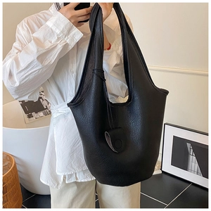 Detail of minimalist black pebbled leather tote bag with wide strap and round charm