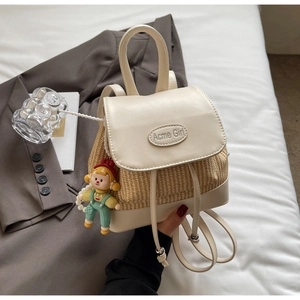 Detail eines beigen Rucksacks aus Kunstleder und Stroh mit buntem Puppenanhänger