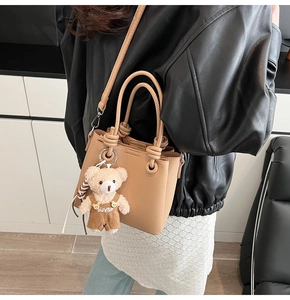 Detailed shot of tan leather bucket bag with knotted handle and teddy bear charm